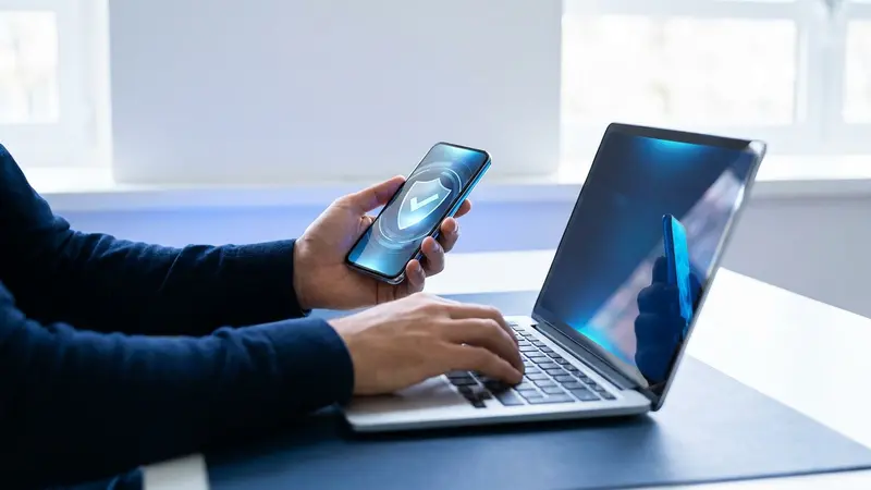 Person signing in on a laptop while approving a multi-factor prompt on their phone